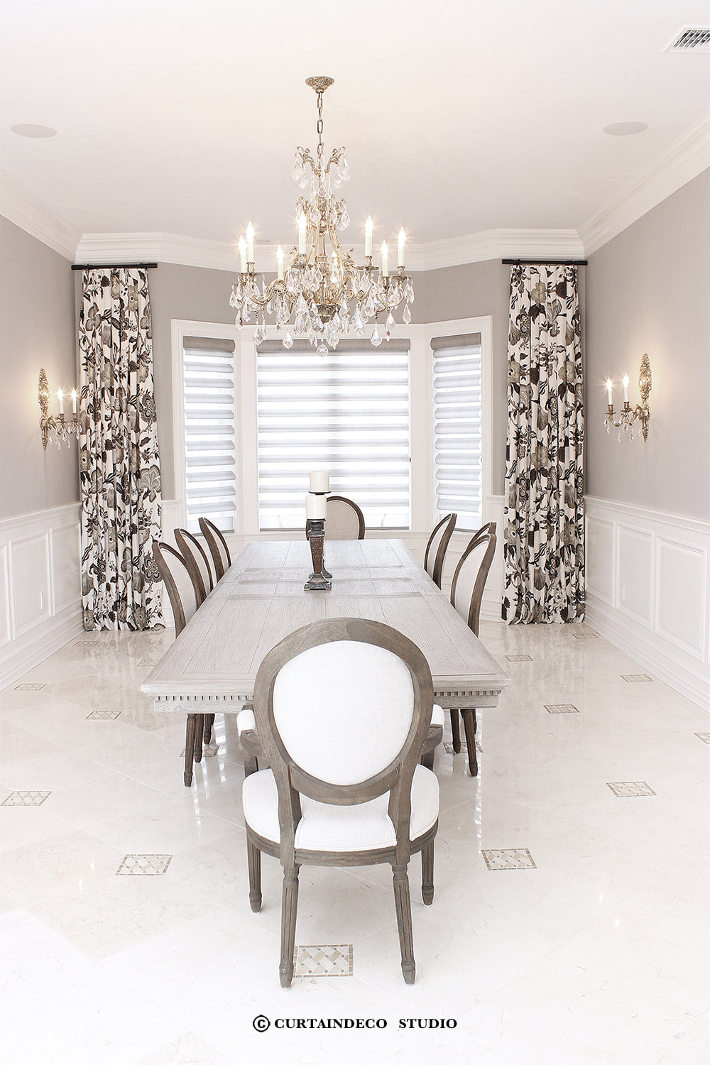 Elegant formal dining room in Demarest, NJ, featuring luxurious patterned curtains flanking a large window with layered shades, complemented by a classic chandelier and refined decor.