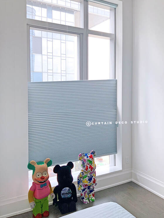 Kids' room with large windows featuring a cellular shade and colorful toys on the floor, providing a playful and cozy environment.