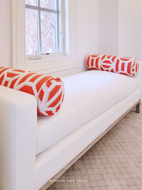 Close-up view of the white bench in Alpine, NJ, with orange and white geometric bolster pillows, showcasing the detailed and vibrant design of the decor.